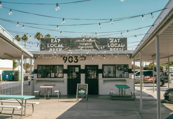 The Arlington Cattle Co storefront at 903 Monroe Ave with Eat Local Beef banners, string lights, and shaded picnic tables